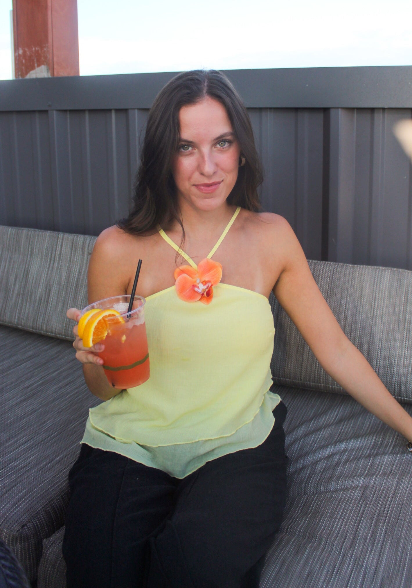 Woman sitting on a couch holding a drink with a straw and orange garnish.