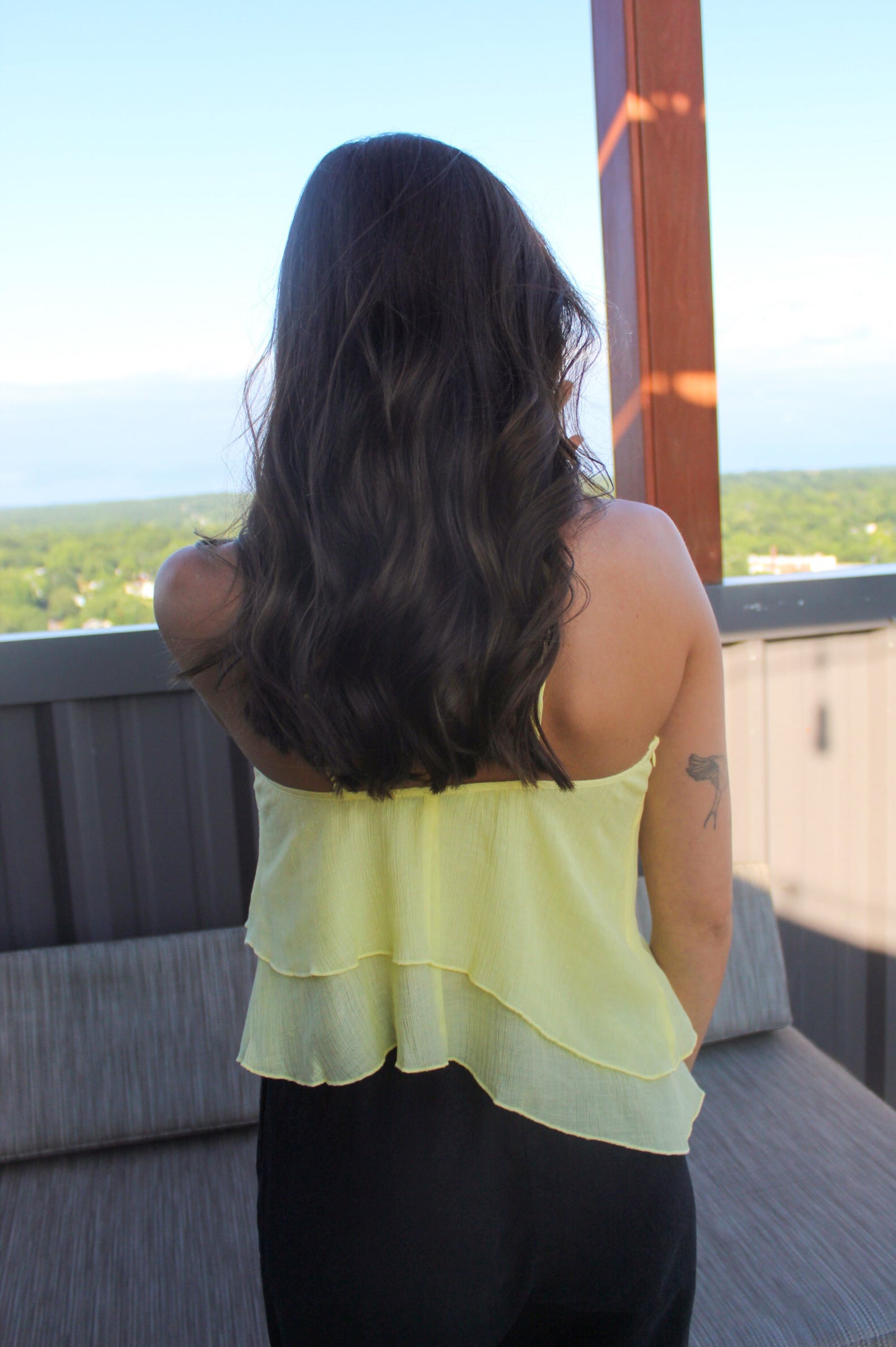 Woman in a yellow top standing on a balcony with a scenic view.