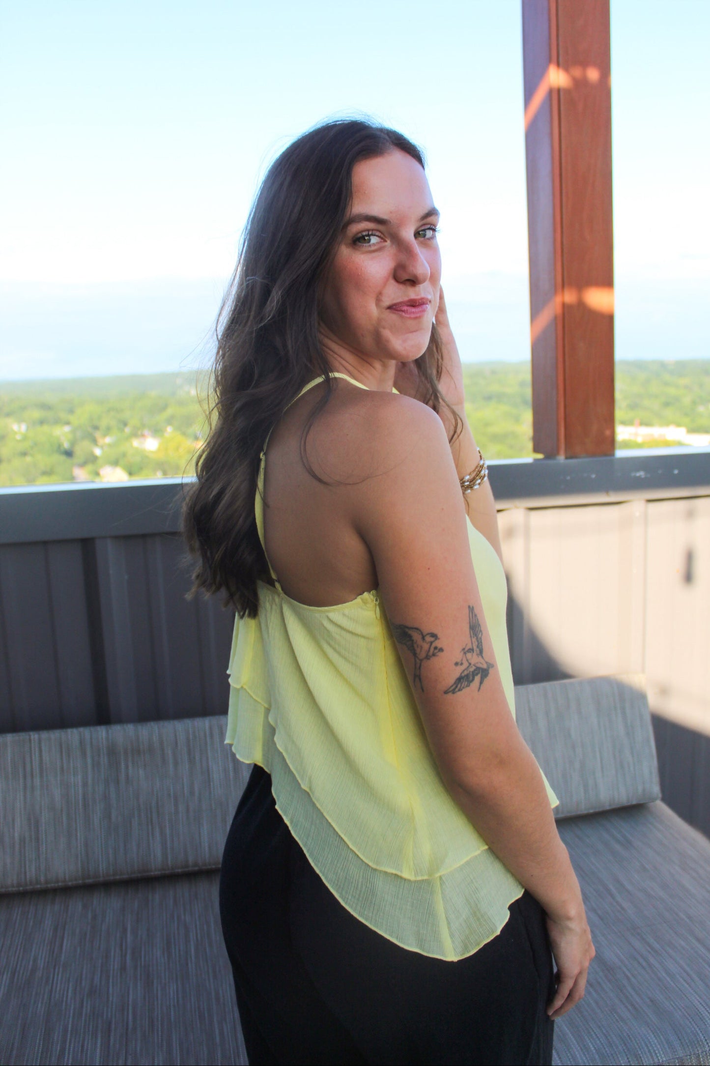Woman in a yellow top standing on a balcony with a scenic view