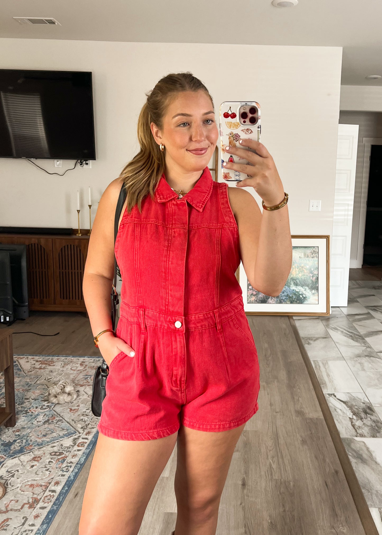 Woman taking a mirror selfie wearing a red romper in a living room.