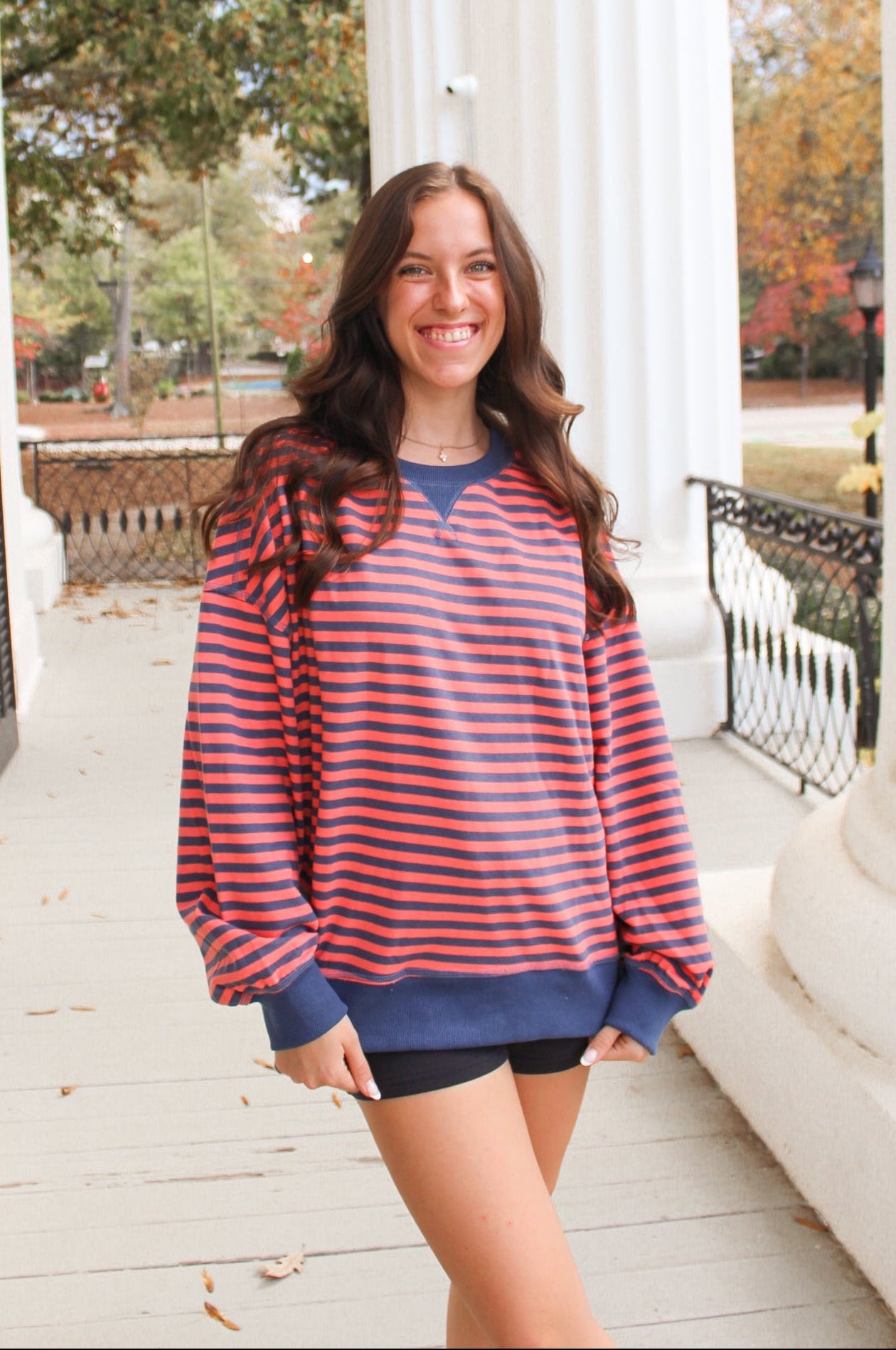 Woman wearing a red and blue striped sweater on a porch with trees in the background