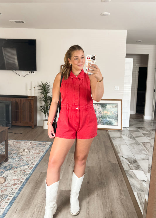 Woman taking a mirror selfie wearing a red romper and white boots in a living room. Front facing picture.